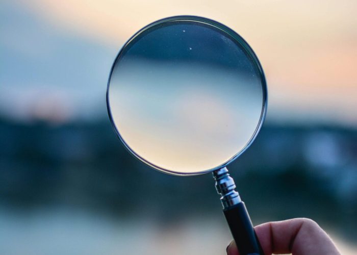 A magnifying glass held by a hand outdoors at sunset, focusing on exploration.